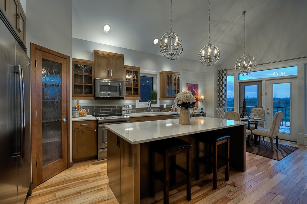 Example of a mid-sized transitional l-shaped medium tone wood floor eat-in kitchen design with an undermount sink, shaker cabinets, medium tone wood cabinets, quartz countertops, brown backsplash, glass tile backsplash, stainless steel appliances and an island