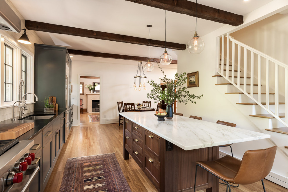 This is an example of a large country l-shaped eat-in kitchen in Portland with an undermount sink, shaker cabinets, blue cabinets, soapstone benchtops, white splashback, subway tile splashback, stainless steel appliances, light hardwood floors, with island and black benchtop.