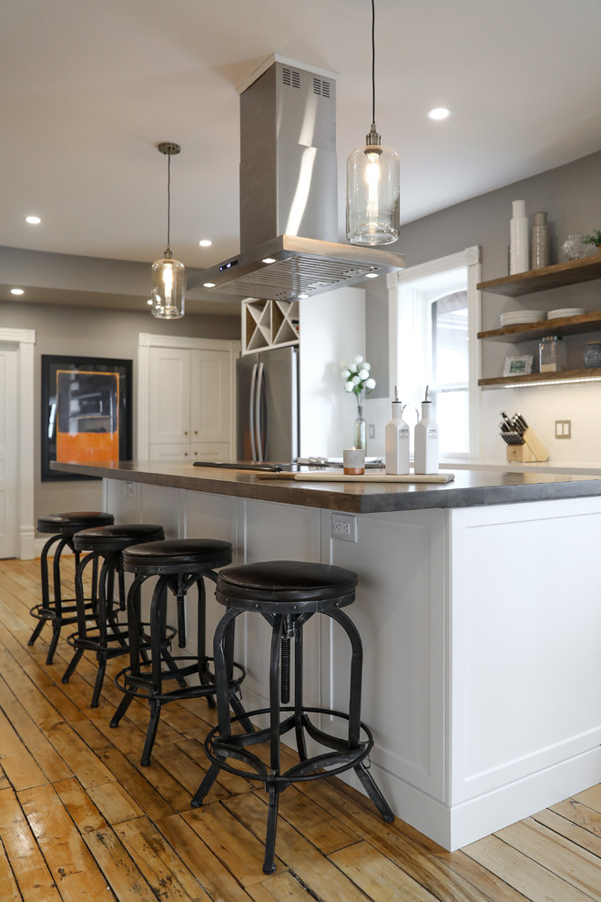 Inspiration for a mid-sized transitional single-wall medium tone wood floor and brown floor eat-in kitchen remodel with a farmhouse sink, shaker cabinets, white cabinets, white backsplash, stainless steel appliances, an island and white countertops