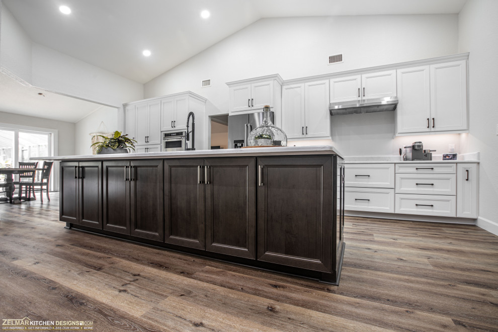 Photo of a mid-sized transitional l-shaped eat-in kitchen in Orlando with an undermount sink, recessed-panel cabinets, white cabinets, quartz benchtops, white splashback, ceramic splashback, vinyl floors, with island, brown floor and white benchtop.