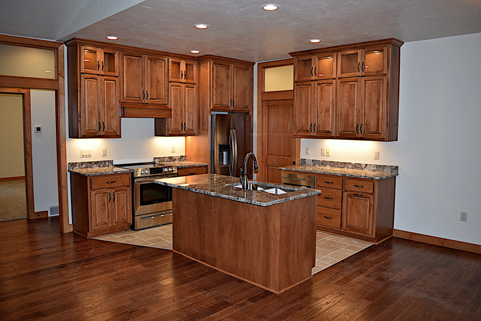 Mid-sized l-shaped open concept kitchen photo with an undermount sink, raised-panel cabinets, granite countertops, ceramic backsplash, stainless steel appliances and an island