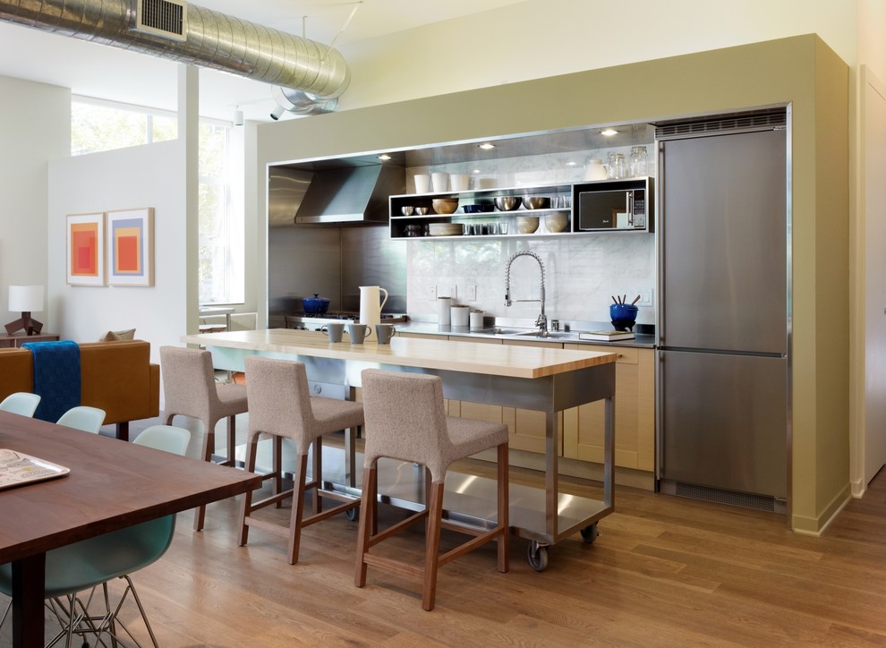 Photo of an industrial single-wall open plan kitchen in Los Angeles with stainless steel benchtops, open cabinets, an integrated sink, stainless steel cabinets, white splashback, stone slab splashback and stainless steel appliances.