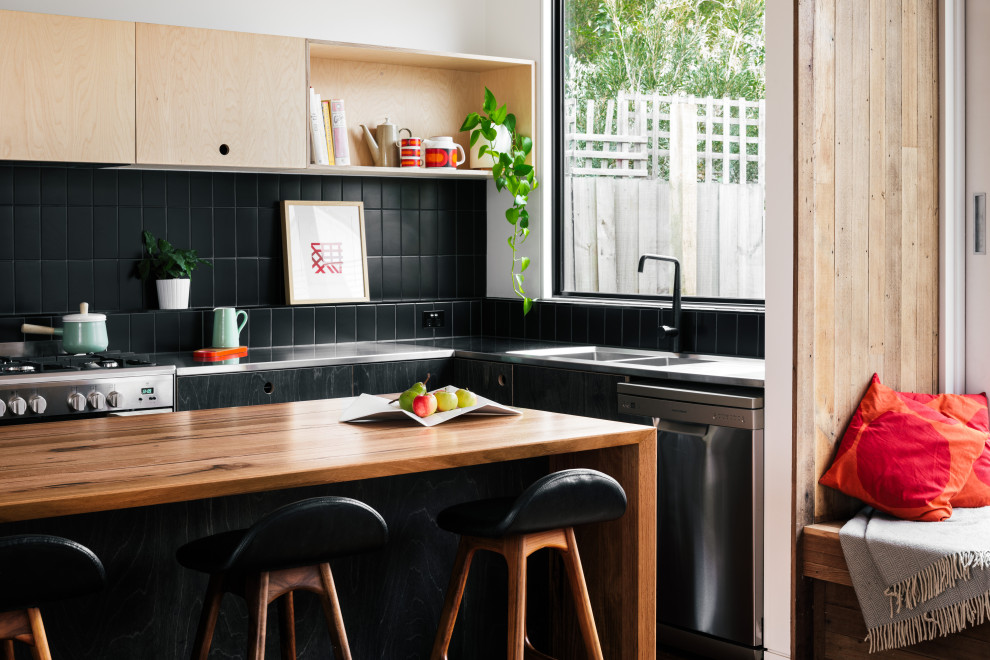Inspiration for a contemporary l-shaped kitchen in Melbourne with an integrated sink, flat-panel cabinets, black cabinets, stainless steel benchtops, black splashback, stainless steel appliances, with island and grey benchtop.