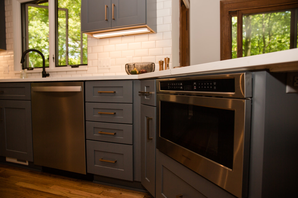 Eat-in kitchen - mid-sized transitional galley medium tone wood floor and white floor eat-in kitchen idea with an undermount sink, shaker cabinets, white cabinets, solid surface countertops, white backsplash, ceramic backsplash, stainless steel appliances, a peninsula and white countertops