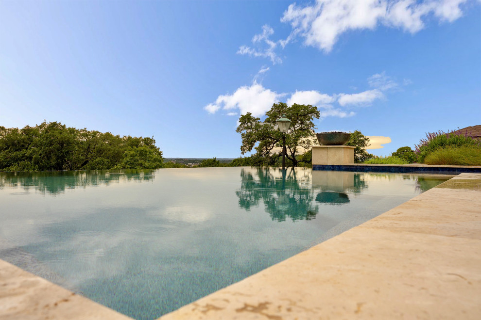 Expansive modern backyard rectangular infinity pool in Austin with with privacy feature and concrete slab.