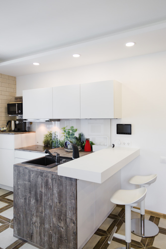 Small contemporary l-shaped kitchen in Other with an undermount sink, white cabinets, laminate benchtops, white splashback, glass sheet splashback, black appliances and grey benchtop.