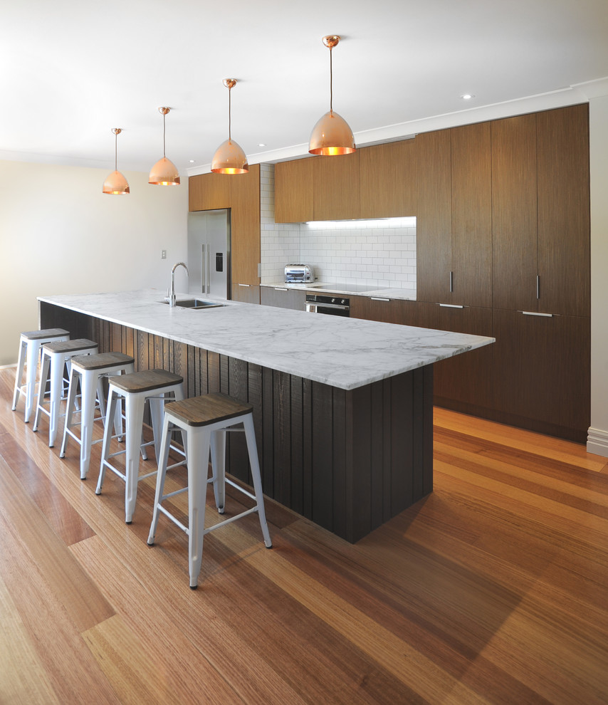 This is an example of a mid-sized modern galley eat-in kitchen in Auckland with an undermount sink, flat-panel cabinets, medium wood cabinets, marble benchtops, white splashback, subway tile splashback, stainless steel appliances, medium hardwood floors and with island.
