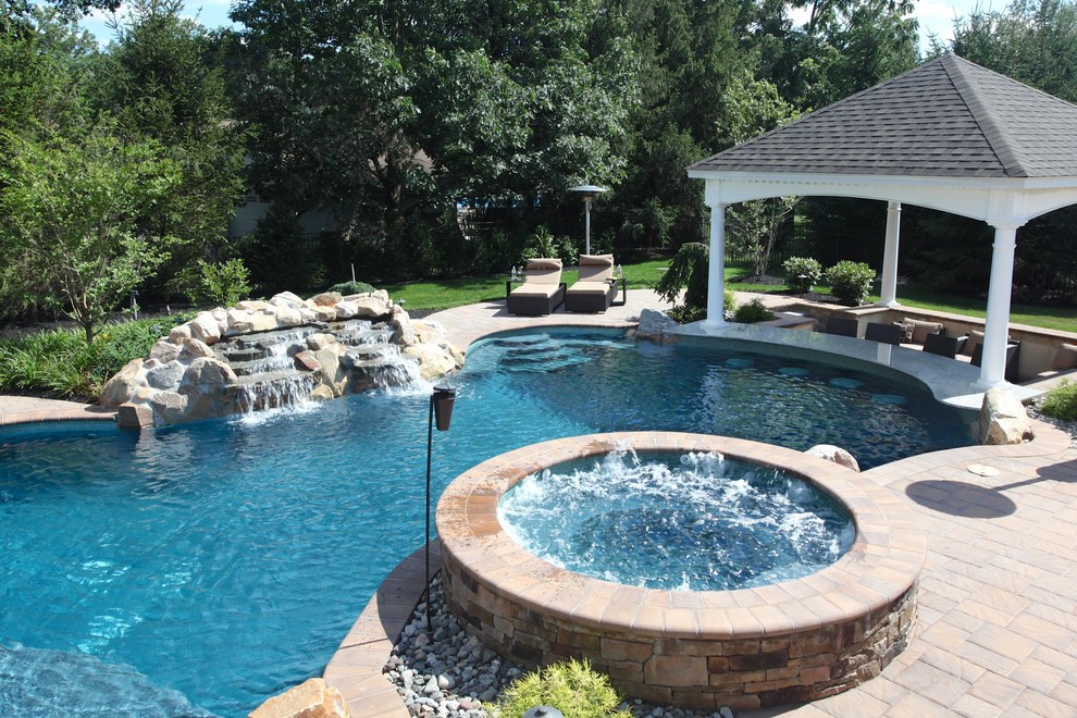 Inspiration for a large tropical backyard custom-shaped pool in New York with a hot tub and concrete pavers.
