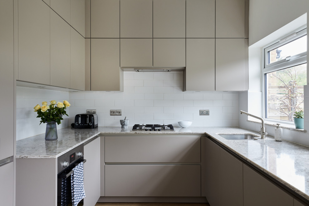 Mid-sized contemporary u-shaped eat-in kitchen in London with an undermount sink, flat-panel cabinets, grey cabinets, quartzite benchtops, white splashback, ceramic splashback, stainless steel appliances, vinyl floors, no island, brown floor and multi-coloured benchtop.