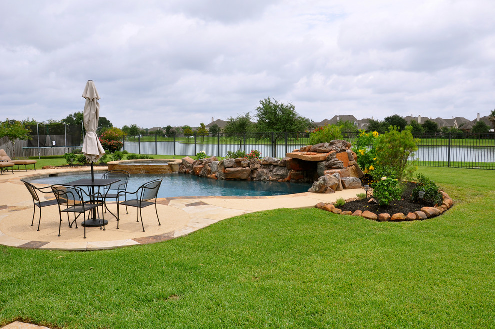 Photo of a large traditional backyard custom-shaped natural pool in Houston with a hot tub and concrete slab.