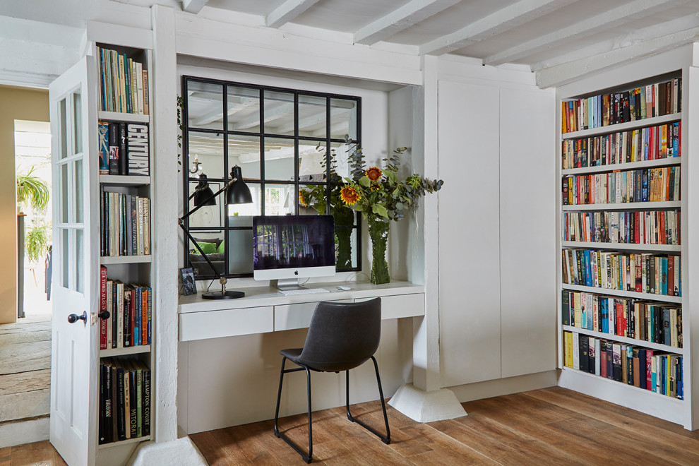 Inspiration for a transitional home office in London with white walls, medium hardwood floors, a built-in desk, brown floor and exposed beam.