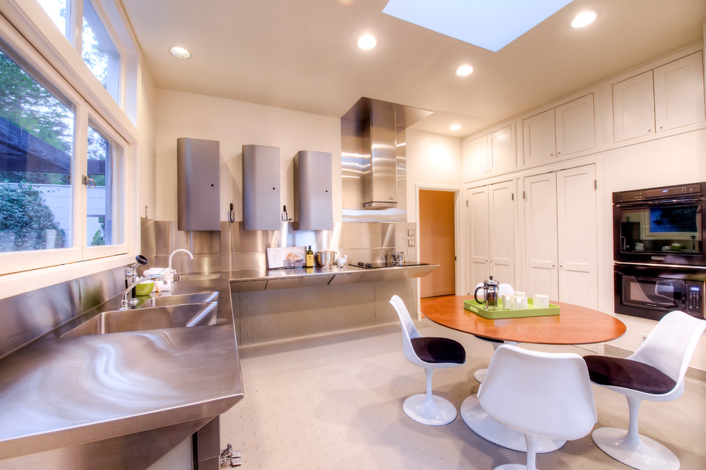 Photo of a large modern l-shaped separate kitchen in San Francisco with an integrated sink, recessed-panel cabinets, white cabinets, stainless steel benchtops, black appliances and no island.