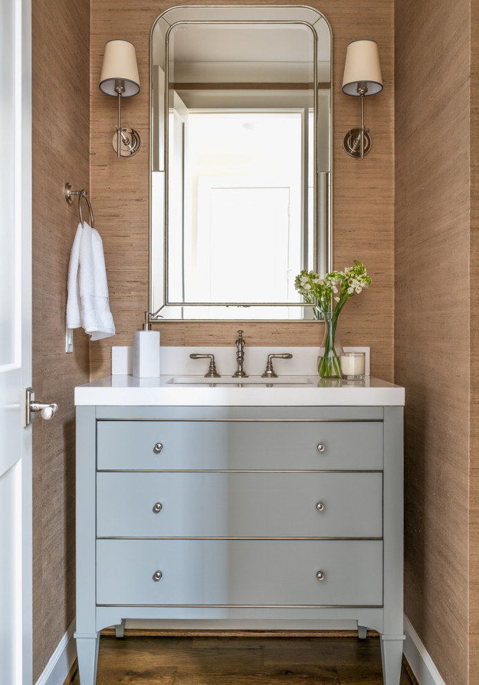 This is an example of a transitional powder room in Birmingham with furniture-like cabinets, blue cabinets, brown walls, medium hardwood floors, an undermount sink, brown floor and white benchtops.