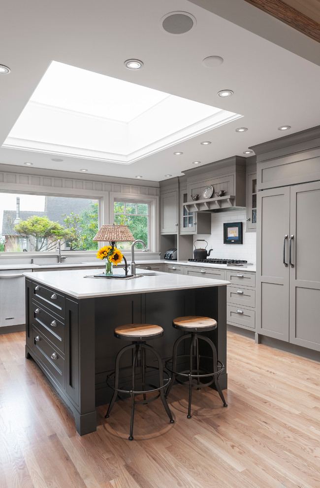 Transitional l-shaped kitchen in Vancouver with shaker cabinets, grey cabinets, white splashback, panelled appliances, light hardwood floors and with island.