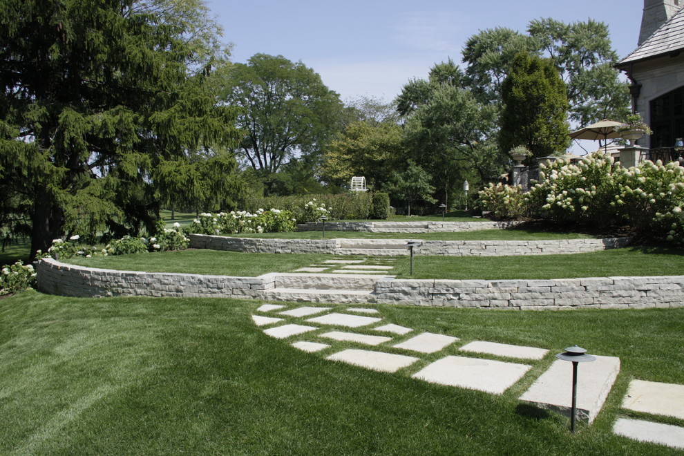 Expansive traditional sloped partial sun garden in Chicago with a retaining wall and natural stone pavers.