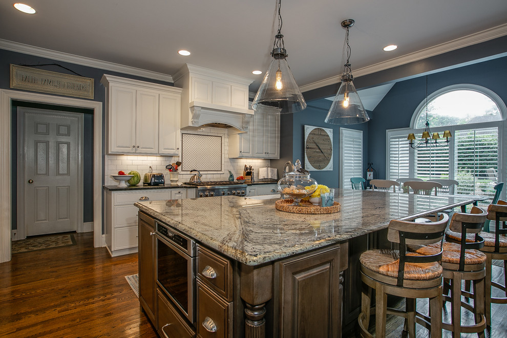 Inspiration for a large transitional l-shaped medium tone wood floor and brown floor open concept kitchen remodel in Charlotte with white cabinets, granite countertops, white backsplash, stainless steel appliances, an island, a farmhouse sink, raised-panel cabinets, porcelain backsplash and white countertops