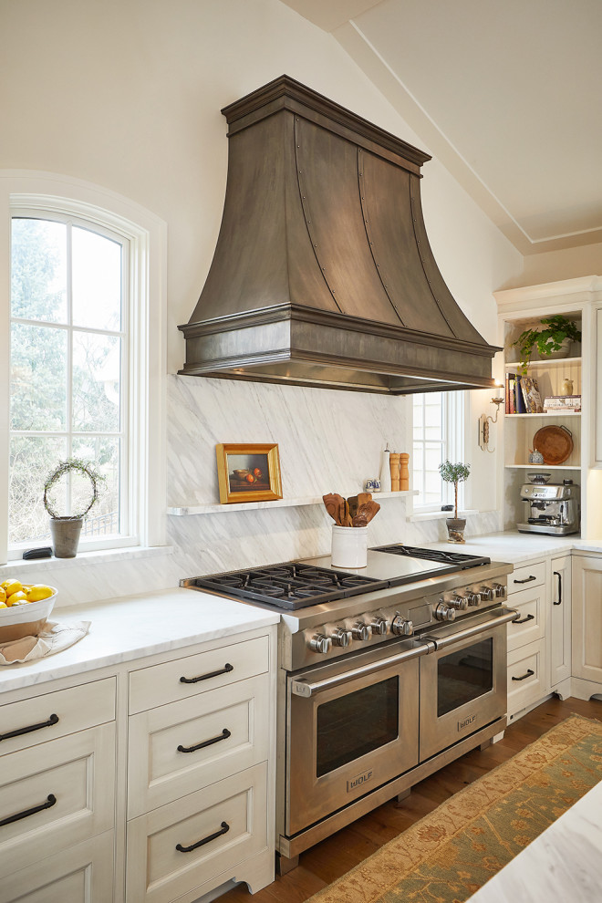 This is an example of an expansive l-shaped eat-in kitchen in Grand Rapids with an undermount sink, recessed-panel cabinets, white cabinets, marble benchtops, white splashback, marble splashback, panelled appliances, light hardwood floors, multiple islands, white floor, white benchtop and vaulted.