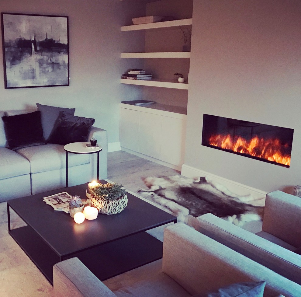 Photo of a mid-sized scandinavian open concept living room in Cheshire with a library, grey walls, light hardwood floors, a wood stove, a plaster fireplace surround and a wall-mounted tv.