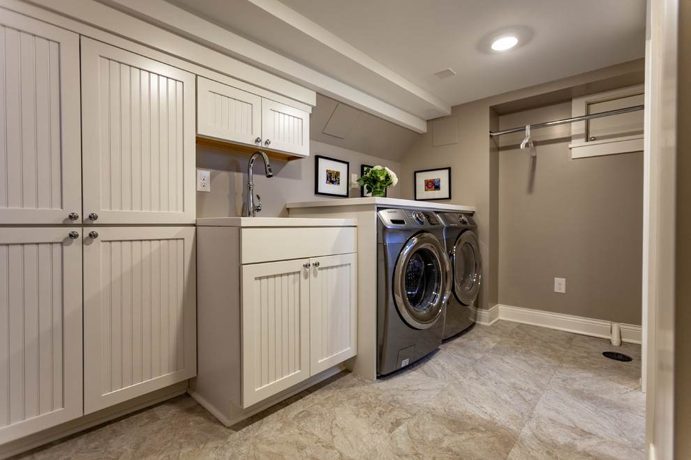 This is an example of a large traditional single-wall dedicated laundry room in Minneapolis with an undermount sink, beaded inset cabinets, white cabinets, marble benchtops, beige walls, vinyl floors, a side-by-side washer and dryer, beige floor and white benchtop.