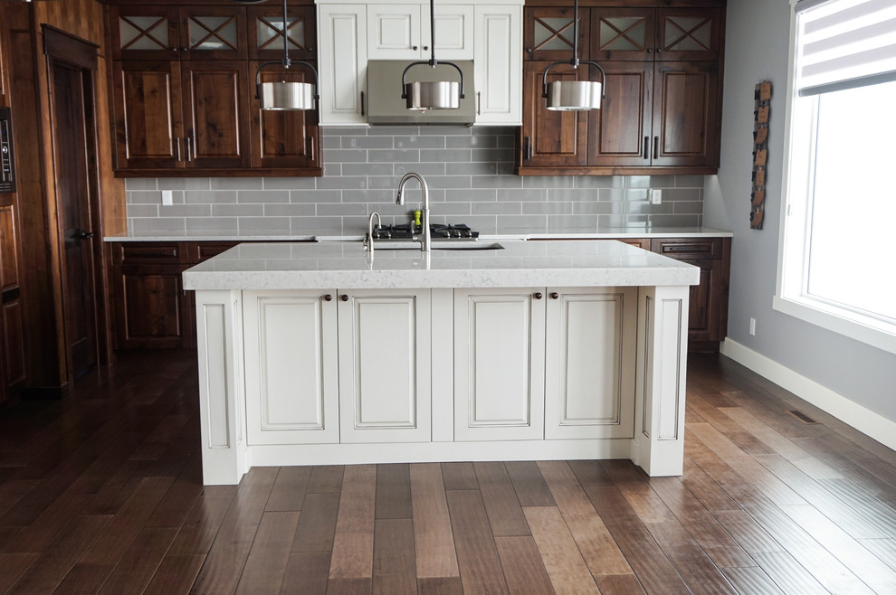 Kitchen pantry - large traditional l-shaped medium tone wood floor and brown floor kitchen pantry idea in Calgary with an undermount sink, raised-panel cabinets, brown cabinets, quartz countertops, gray backsplash, ceramic backsplash, stainless steel appliances, an island and white countertops