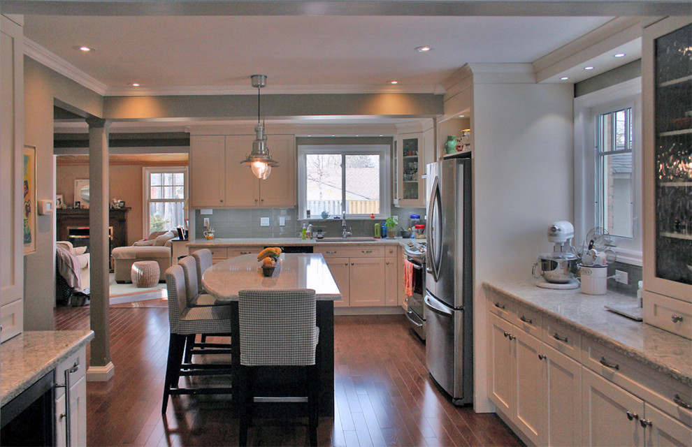 Large transitional l-shaped medium tone wood floor eat-in kitchen photo in Toronto with an undermount sink, shaker cabinets, white cabinets, quartz countertops, gray backsplash, glass tile backsplash, stainless steel appliances and an island