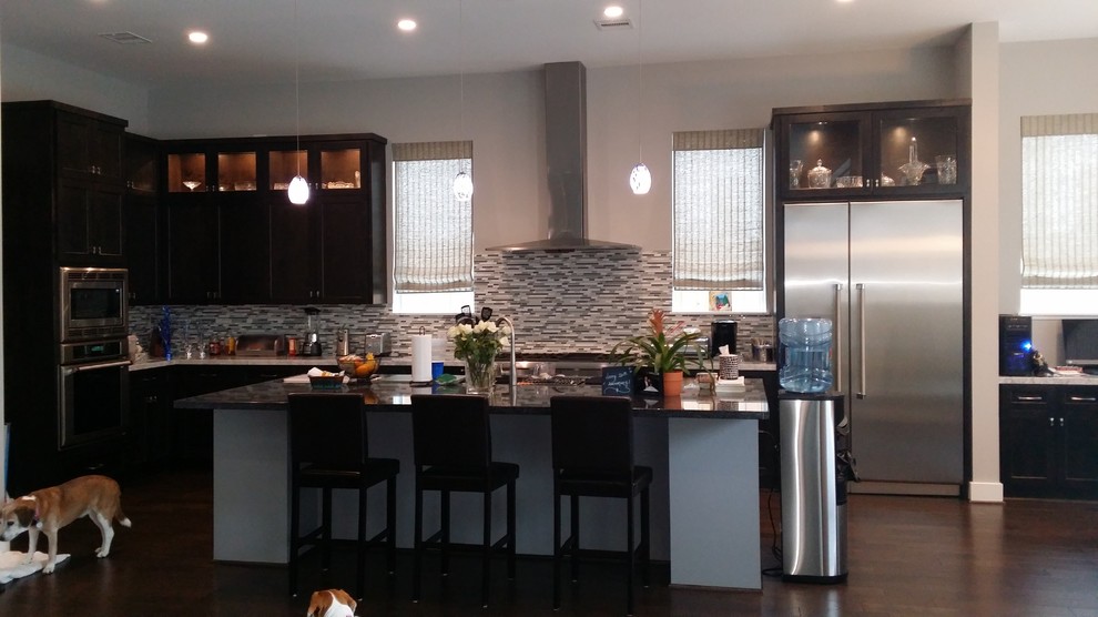Inspiration for a large transitional l-shaped dark wood floor and brown floor open concept kitchen remodel in Houston with dark wood cabinets, granite countertops, an island, an undermount sink, gray backsplash, matchstick tile backsplash and stainless steel appliances