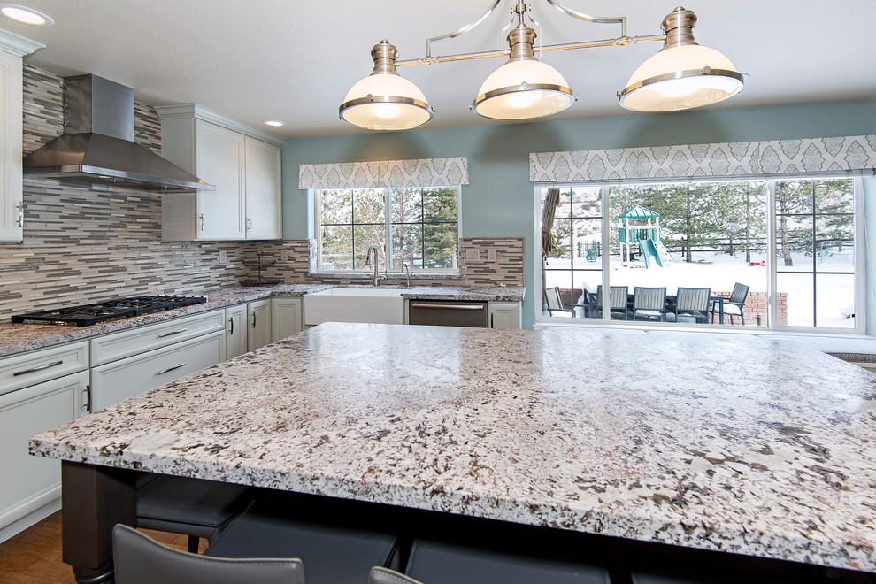 Example of a large transitional medium tone wood floor enclosed kitchen design with a farmhouse sink, recessed-panel cabinets, white cabinets, granite countertops, multicolored backsplash, matchstick tile backsplash, stainless steel appliances and an island