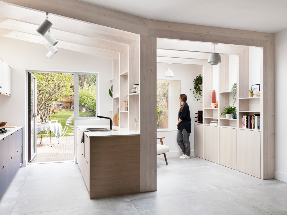Mid-sized scandinavian galley open plan kitchen in London with a drop-in sink, flat-panel cabinets, blue cabinets, solid surface benchtops, white splashback, granite splashback, black appliances, porcelain floors, no island, grey floor, white benchtop and exposed beam.