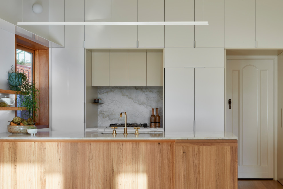 This is an example of a small contemporary galley kitchen/diner in Melbourne with a double-bowl sink, flat-panel cabinets, beige cabinets, marble worktops, beige splashback, marble splashback, stainless steel appliances, medium hardwood flooring, no island, brown floors and beige worktops.