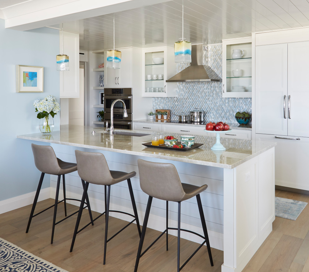 Photo of a mid-sized beach style galley open plan kitchen with an undermount sink, shaker cabinets, white cabinets, quartzite benchtops, multi-coloured splashback, glass tile splashback, panelled appliances, medium hardwood floors, a peninsula, brown floor, grey benchtop and timber.