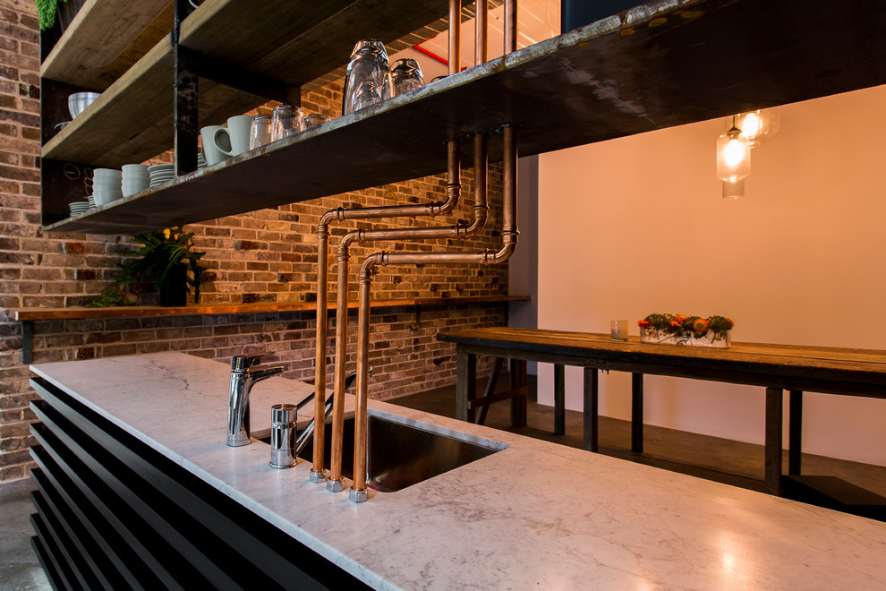 Mid-sized industrial single-wall eat-in kitchen in Sydney with a drop-in sink, open cabinets, stainless steel appliances and concrete floors.