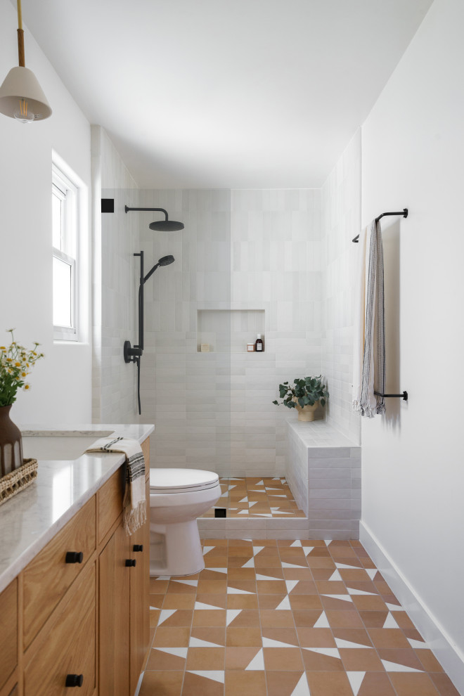 Photo of a coastal bathroom in Los Angeles with flat-panel cabinets, medium wood cabinets, an alcove shower, white tiles, white walls, a submerged sink, orange floors, an open shower, white worktops, a wall niche and a shower bench.