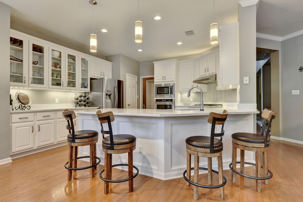Eat-in kitchen - mid-sized transitional u-shaped light wood floor eat-in kitchen idea in Austin with an undermount sink, white cabinets, quartz countertops, white backsplash, stone slab backsplash, stainless steel appliances, a peninsula and raised-panel cabinets