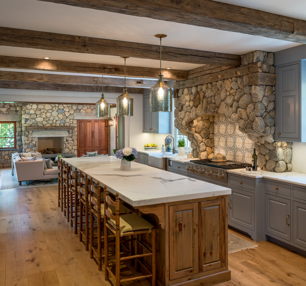 This is an example of a mid-sized traditional open plan kitchen in New York with a farmhouse sink, raised-panel cabinets, marble benchtops, panelled appliances, with island, white benchtop, grey cabinets, multi-coloured splashback, medium hardwood floors and brown floor.