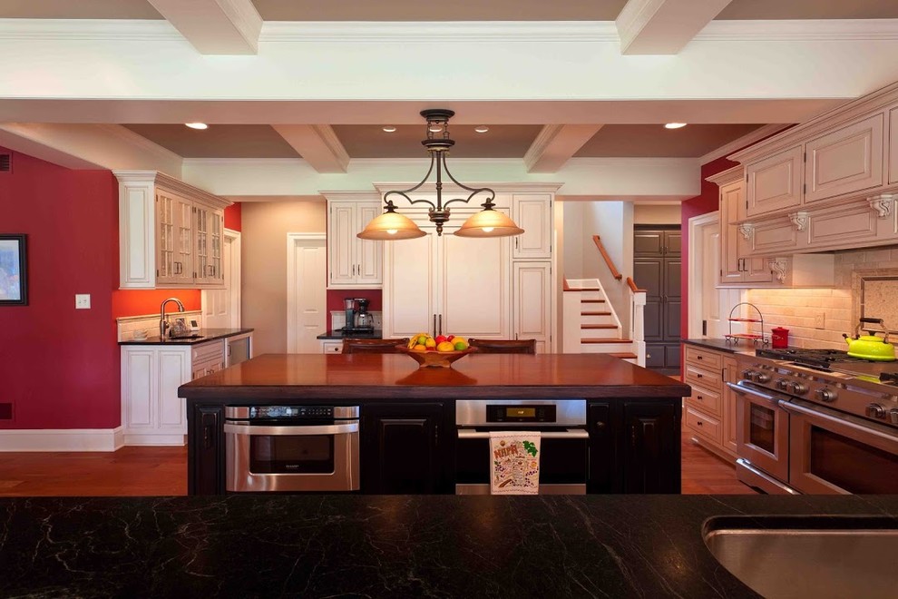 Inspiration for a mid-sized transitional u-shaped medium tone wood floor eat-in kitchen remodel with raised-panel cabinets, white cabinets, soapstone countertops, beige backsplash, ceramic backsplash, stainless steel appliances and an island