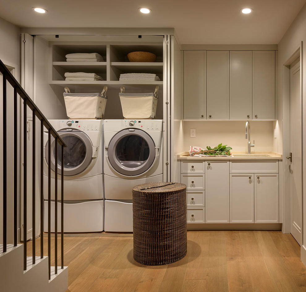 Design ideas for a mid-sized transitional single-wall dedicated laundry room in San Francisco with an undermount sink, recessed-panel cabinets, grey cabinets, limestone benchtops, grey walls, medium hardwood floors, a side-by-side washer and dryer and beige benchtop.