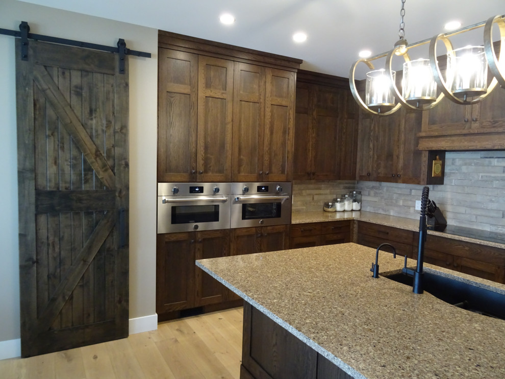 Large transitional l-shaped light wood floor and brown floor kitchen pantry photo with an undermount sink, shaker cabinets, medium tone wood cabinets, granite countertops, gray backsplash, subway tile backsplash, stainless steel appliances, an island and multicolored countertops