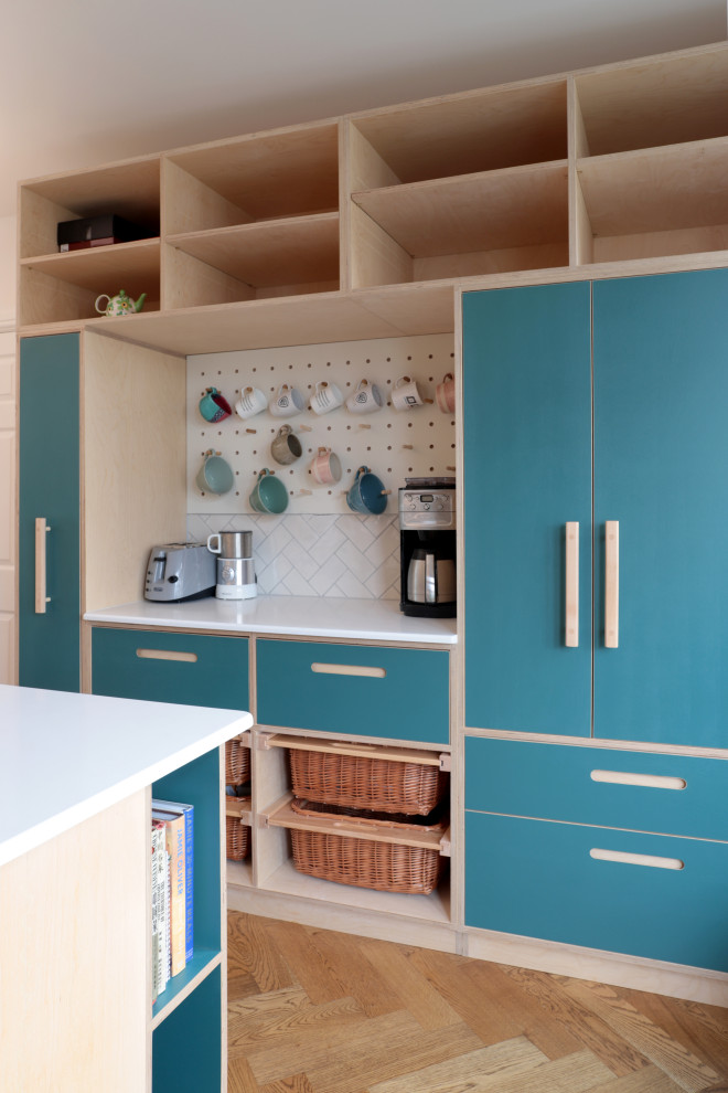 Inspiration for a large scandinavian galley open plan kitchen in London with a double-bowl sink, flat-panel cabinets, turquoise cabinets, white splashback, ceramic splashback, stainless steel appliances, medium hardwood floors, with island, brown floor and white benchtop.