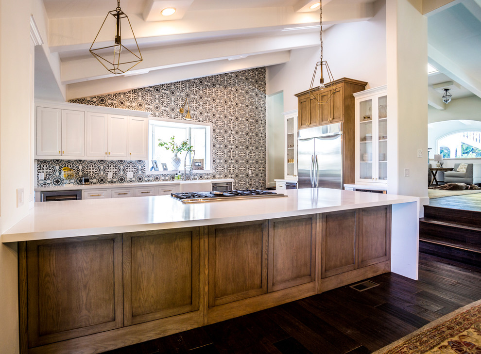 Inspiration for a large transitional u-shaped eat-in kitchen in Los Angeles with a farmhouse sink, shaker cabinets, white cabinets, quartzite benchtops, multi-coloured splashback, ceramic splashback, stainless steel appliances, medium hardwood floors, a peninsula, brown floor and white benchtop.