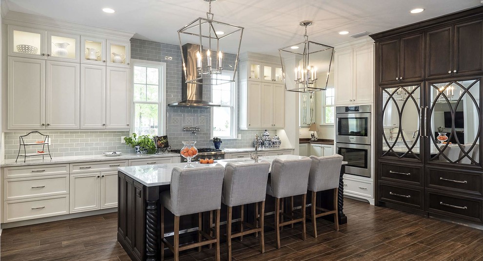 Example of a large transitional l-shaped porcelain tile and brown floor open concept kitchen design with recessed-panel cabinets, white cabinets, an island, an undermount sink, quartz countertops, gray backsplash, subway tile backsplash, stainless steel appliances and white countertops