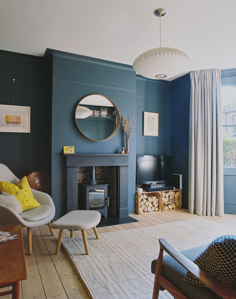 Small contemporary formal enclosed living room in London with blue walls, light hardwood floors, a wood stove, a brick fireplace surround and a corner tv.