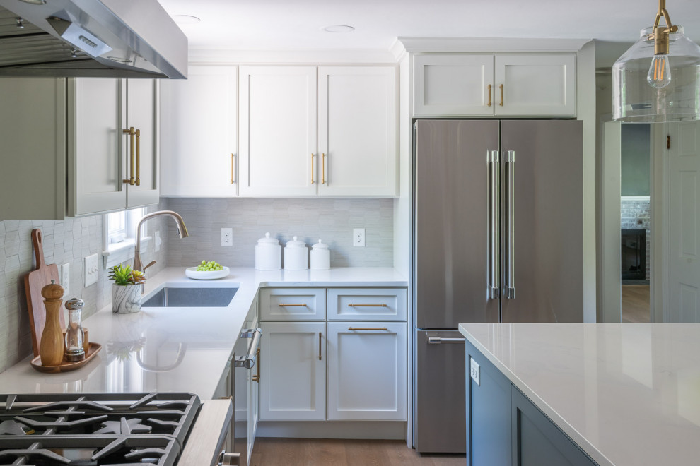 Eat-in kitchen - mid-sized transitional l-shaped light wood floor and brown floor eat-in kitchen idea in Boston with an undermount sink, shaker cabinets, white cabinets, quartz countertops, gray backsplash, ceramic backsplash, stainless steel appliances, an island and white countertops