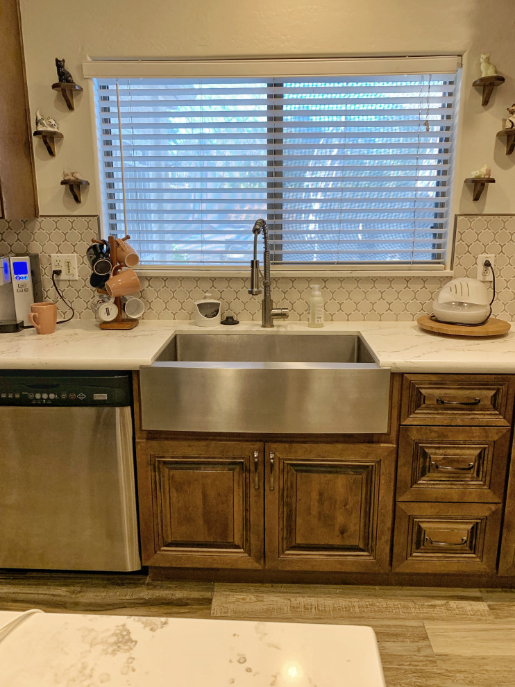 Mid-sized traditional l-shaped open plan kitchen in Phoenix with a farmhouse sink, raised-panel cabinets, distressed cabinets, quartz benchtops, white splashback, glass sheet splashback, stainless steel appliances, ceramic floors, with island, beige floor and white benchtop.
