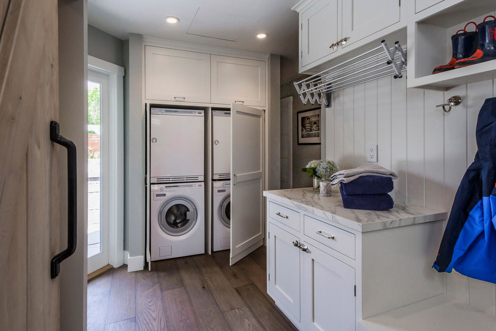This is an example of a large transitional galley utility room in San Francisco with shaker cabinets, white cabinets, grey walls, dark hardwood floors and a stacked washer and dryer.