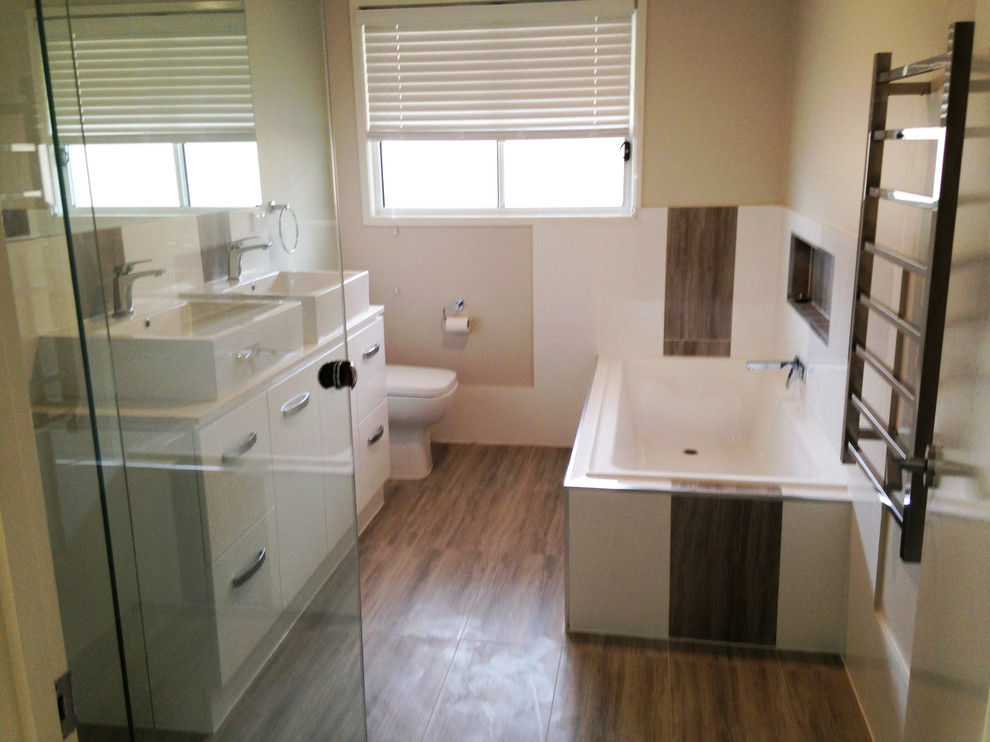 Photo of a mid-sized modern master bathroom in Brisbane with flat-panel cabinets, white cabinets, a corner tub, a corner shower, a two-piece toilet, brown tile, white tile, porcelain tile, beige walls, ceramic floors, a vessel sink, granite benchtops, brown floor and a hinged shower door.