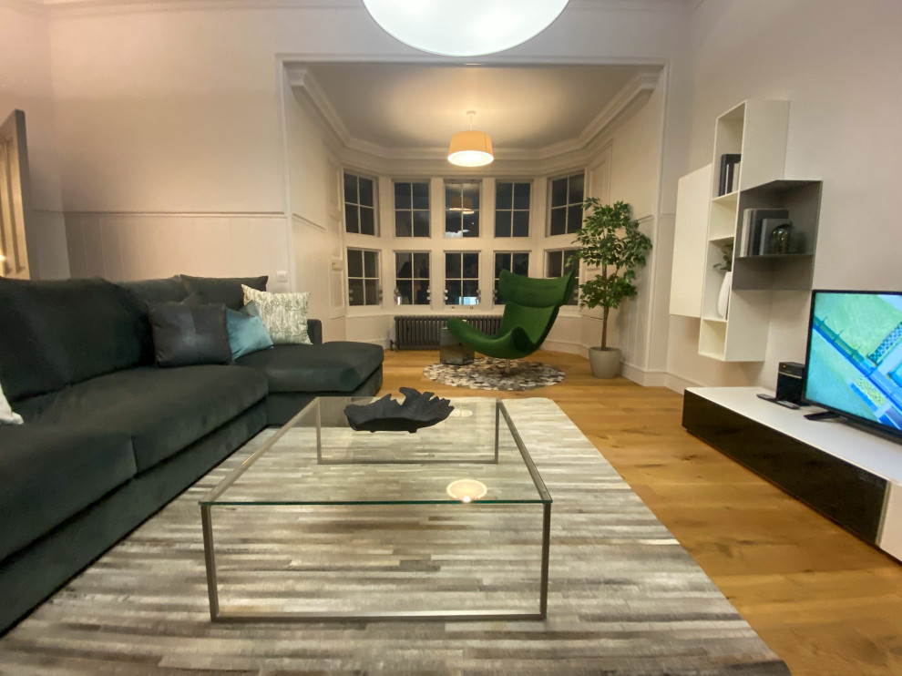 This is an example of a mid-sized contemporary open concept living room in Edinburgh with white walls, carpet, a freestanding tv and beige floor.