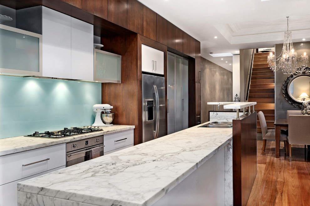 Photo of a contemporary galley eat-in kitchen in Melbourne with flat-panel cabinets, white cabinets, blue splashback and stainless steel appliances.