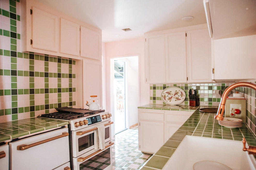 This is an example of a mid-sized eclectic galley open plan kitchen in Los Angeles with shaker cabinets, pink cabinets, tile benchtops, green splashback, ceramic splashback, white appliances, ceramic floors, green floor and green benchtop.