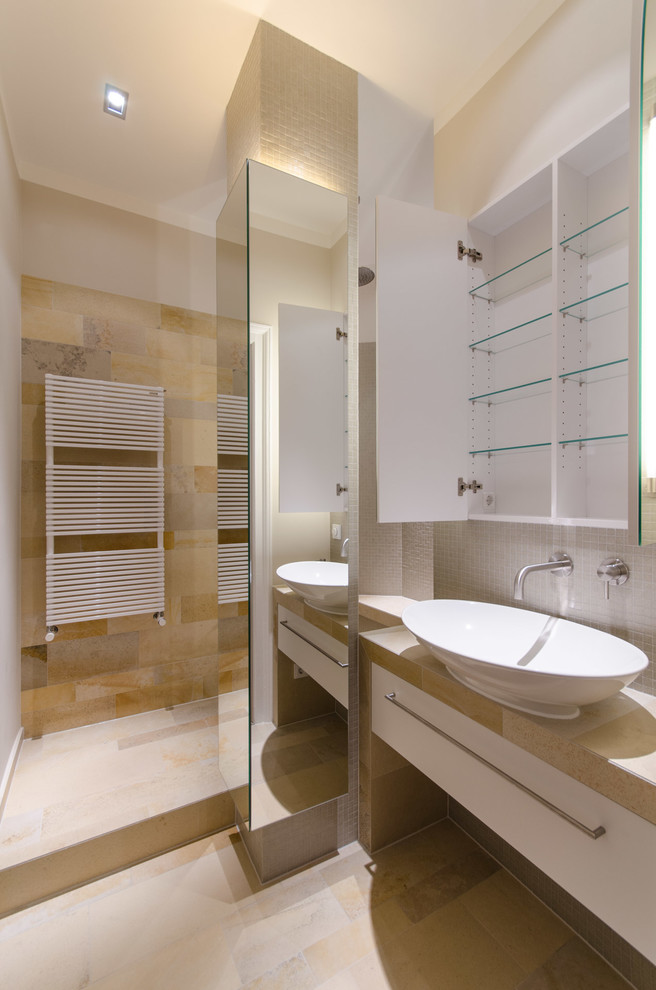 Duschbad mit flächenbündigen Schrankfronten, weißen Schränken, offener Dusche, Wandtoilette, beigen Fliesen, Kalkfliesen, beiger Wandfarbe, Kalkstein, Aufsatzwaschbecken, Kalkstein-Waschbecken/Waschtisch und beigem Boden in Munich