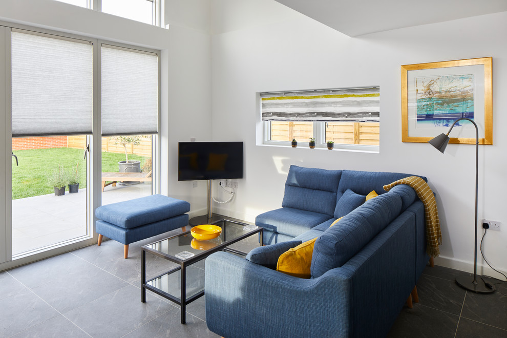 Photo of a modern living room with white walls, slate flooring, a freestanding tv and grey floors.